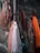 Several fishing nets in various colors including orange, red, and white are hanging against a rough stone wall. Some nets have floats attached, and ropes are tangled among them.