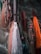 Several fishing nets in various colors including orange, red, and white are hanging against a rough stone wall. Some nets have floats attached, and ropes are tangled among them.