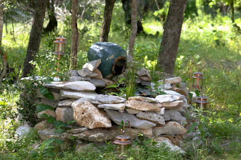 Кафяво‑сива каменна чешма, заобиколена от естествен каменен алпинеум в градина в Батак през деня