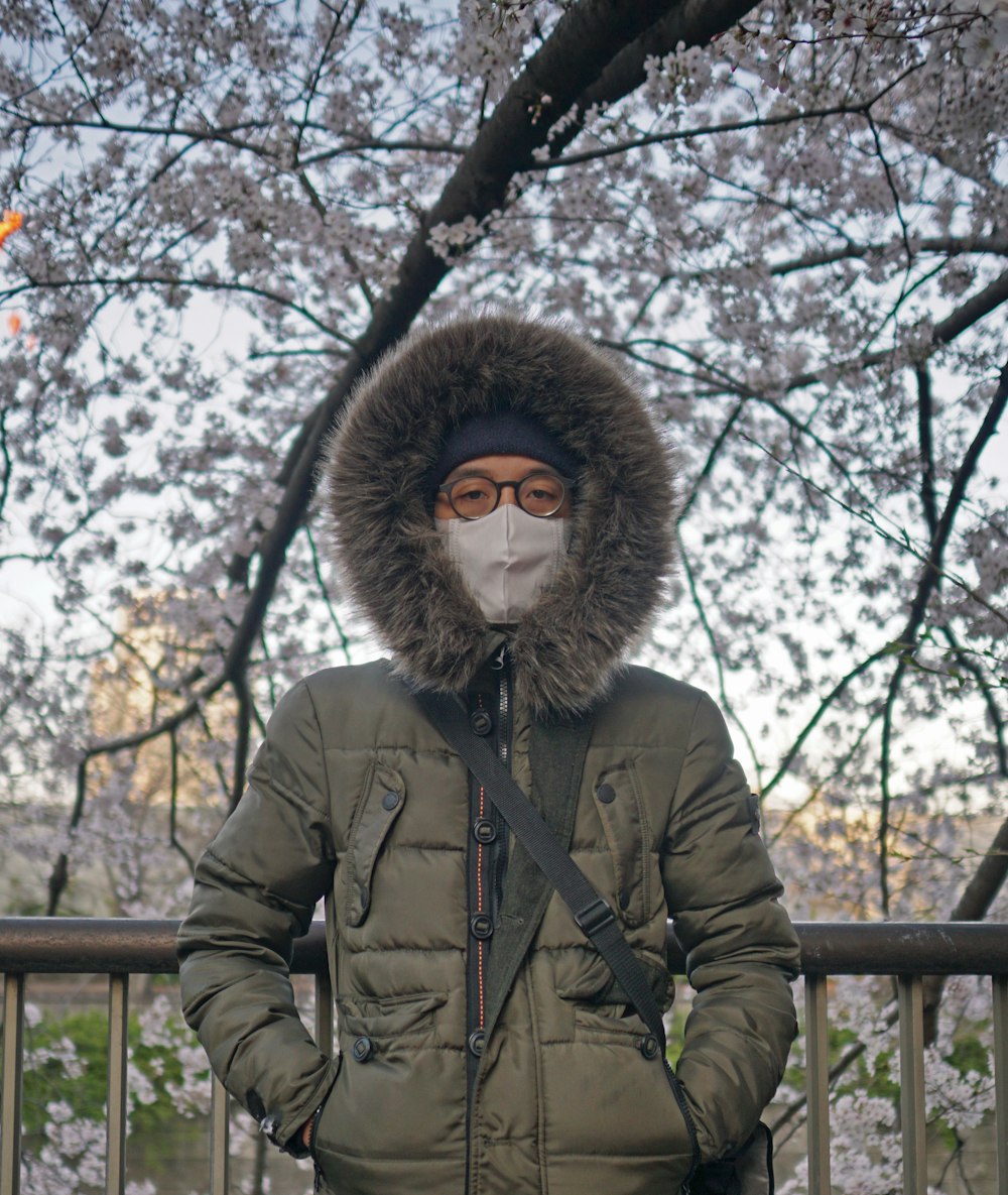 Persona con chaqueta de parka marrón de pie cerca de la valla de madera marrón durante el día