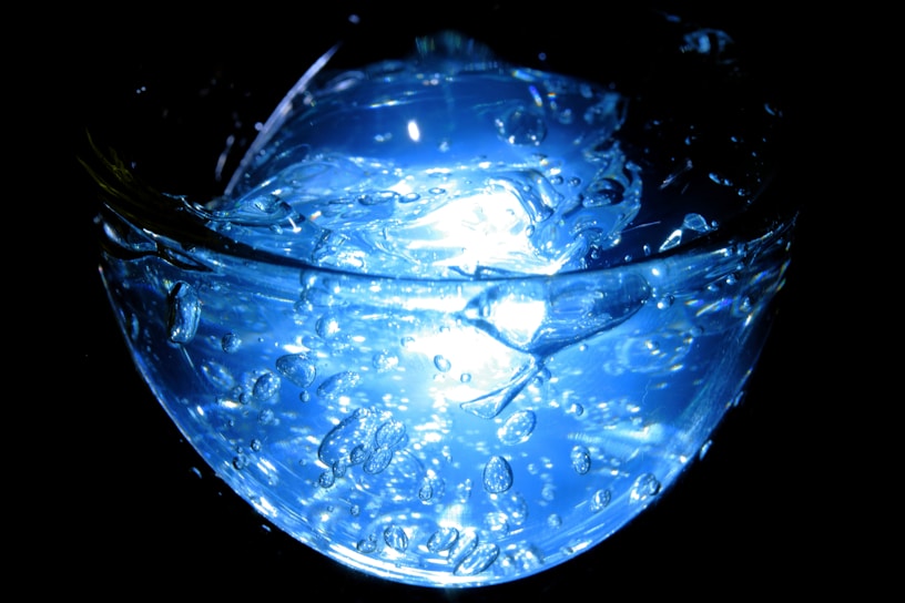 Close-up of bubbling hydroxide solution in a glass beaker emitting faint glowing light.