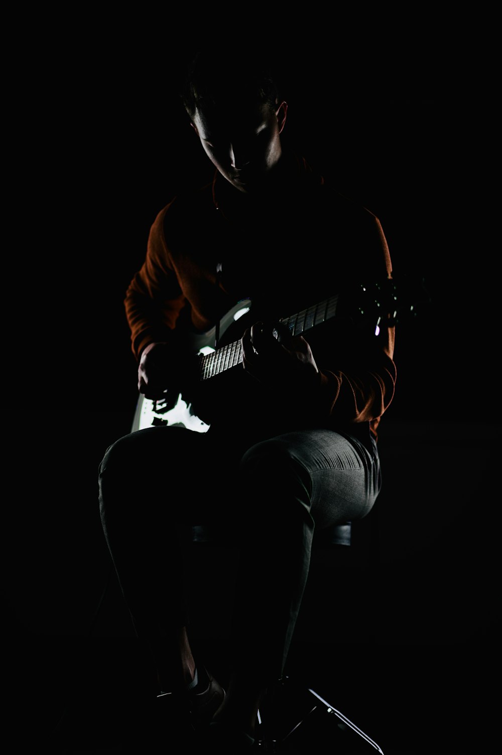 woman in brown leather jacket and blue denim jeans holding white and black stratocaster electric guitar