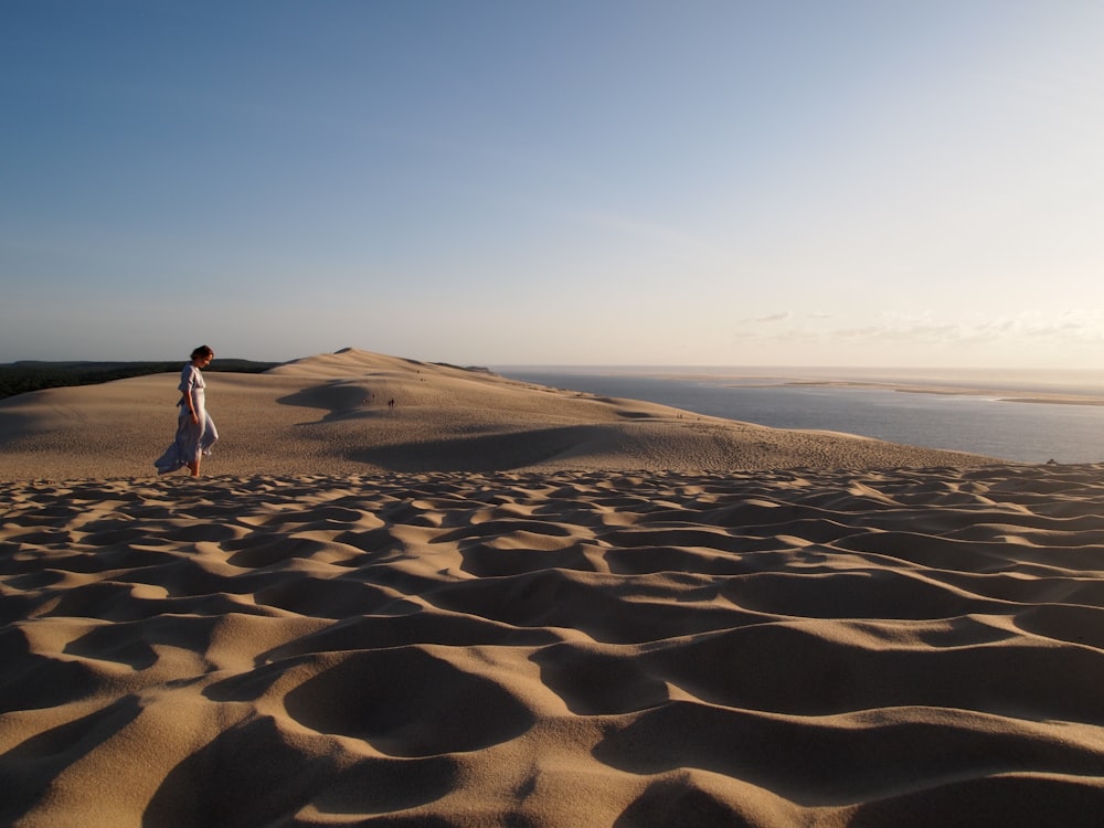 Frau in weißem Kleid, die tagsüber auf braunem Sand spazieren geht