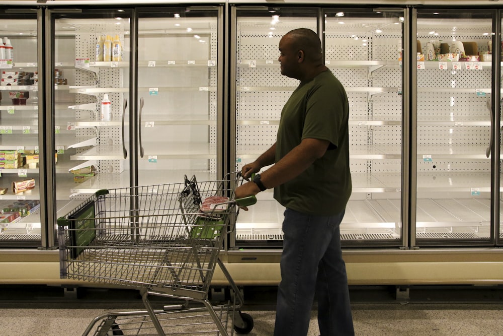 man in brown polo shirt and gray pants standing beside shopping cart