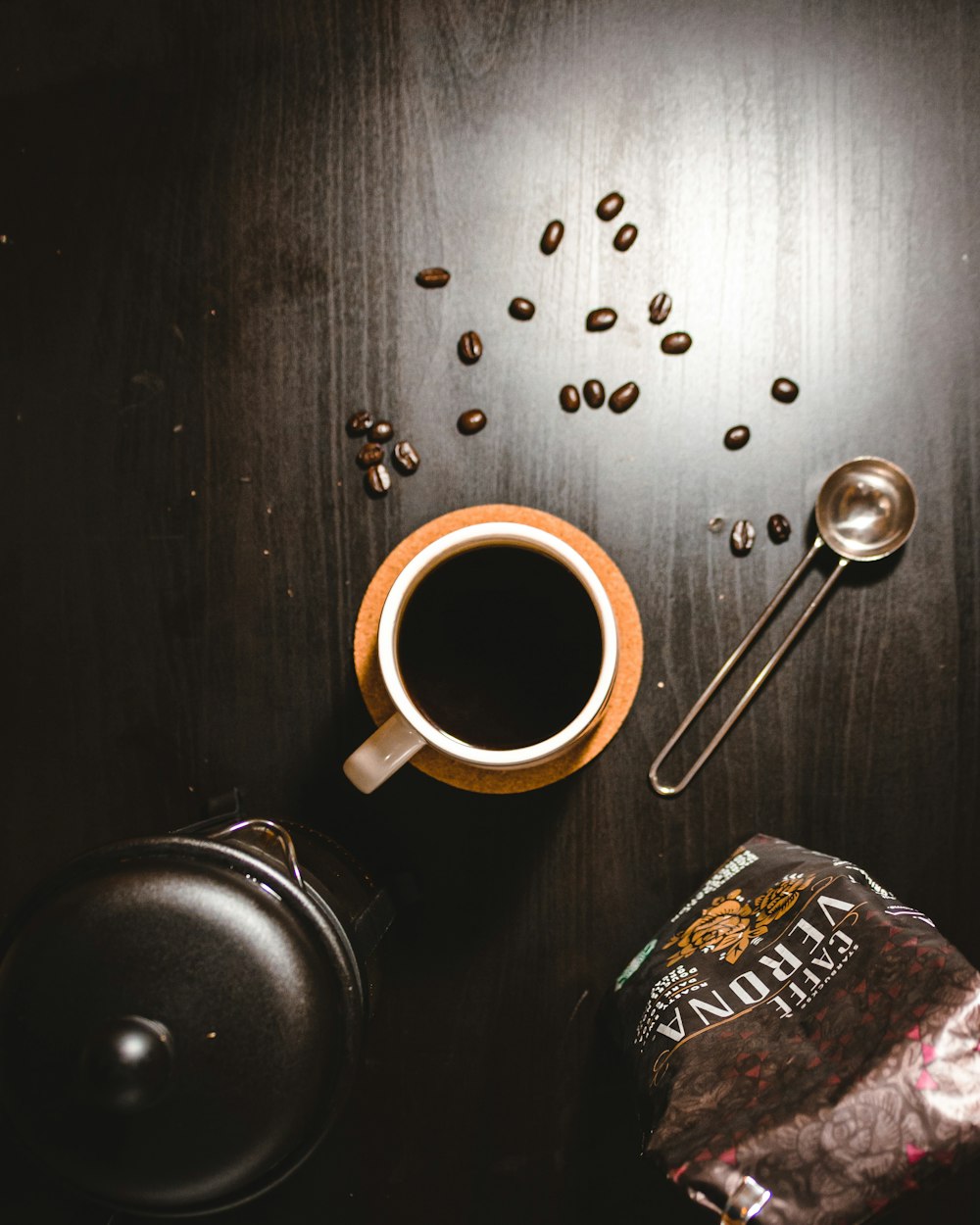 white ceramic mug with coffee beside stainless steel spoon