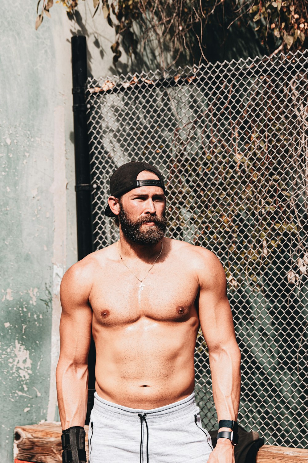 topless man wearing black sunglasses standing beside gray metal fence