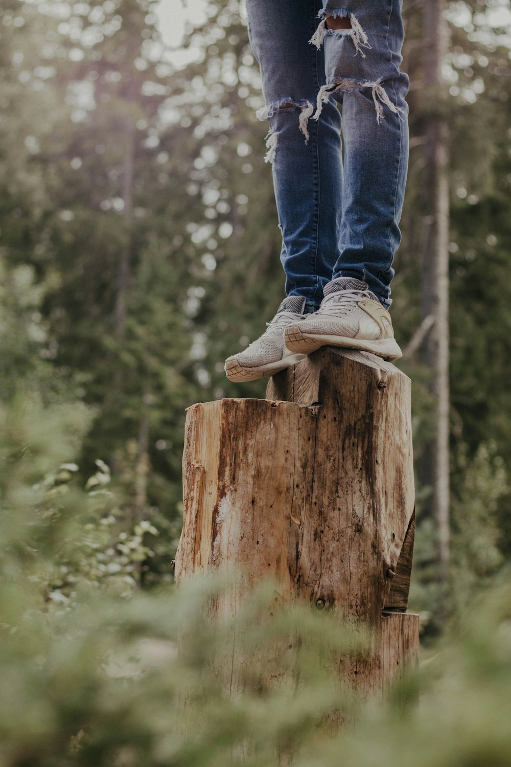 person in blue denim jeans and white sneakers standing on brown wood log