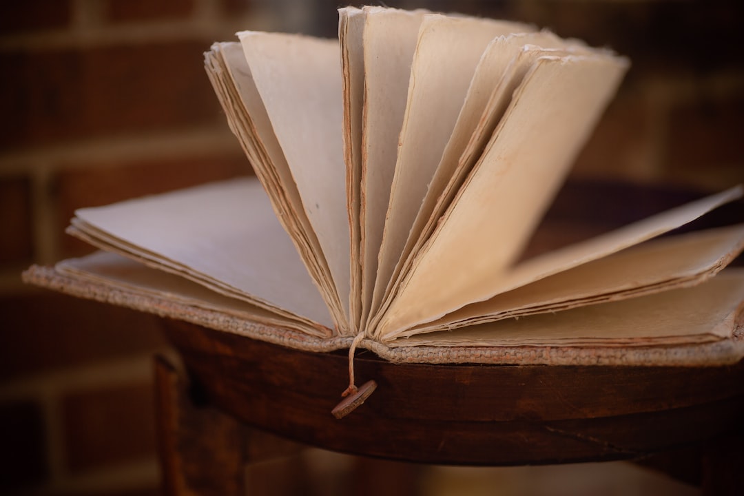 white book on brown wooden table, Vintage deckled edge book journal pages open with page holder and button sitting on chair