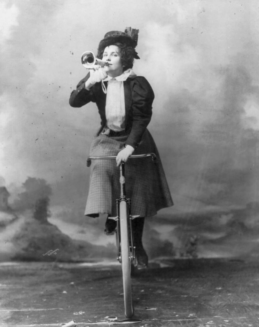 Madge Lessing, full length, on bicycle, holding musical horn to lips
