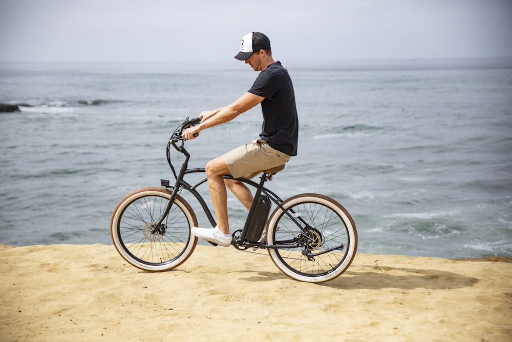 man in black shirt riding on black bicycle near sea during daytime