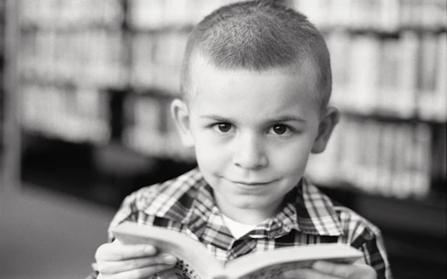 Close-up candid moment of a child flipping pages with a joyful smile in charcoal-toned lighting.