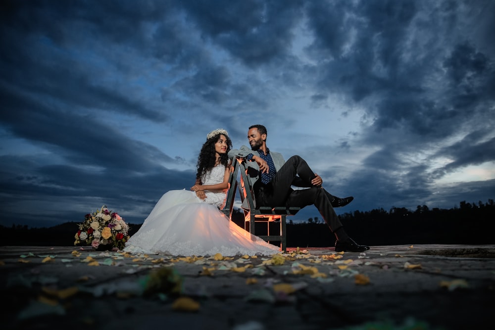 man and woman sitting on bench under cloudy sky during daytime
