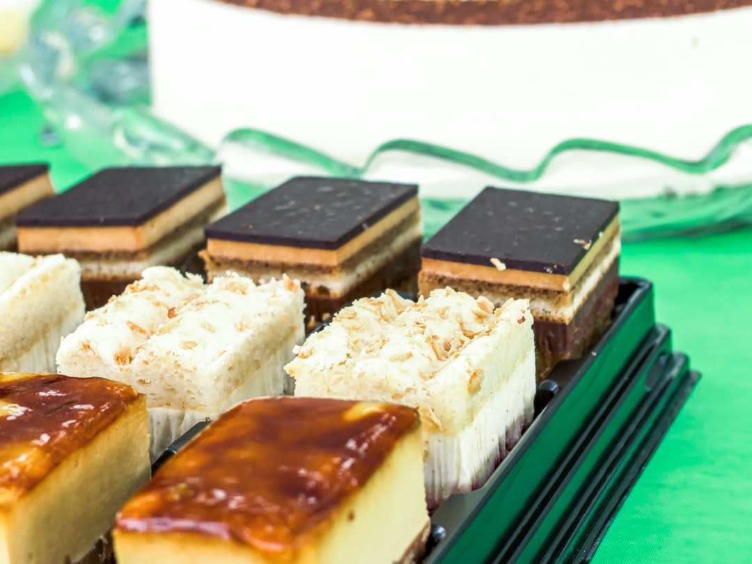 Different flavors of Tiramisu in a black topless container rest on a green table with a cake in the background. 