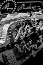 An intricate assembly of metallic gears and mechanical components with detailed reflections on a glossy surface. The scene includes circular cogs and patterns, suggesting a focus on machinery or a mechanical design project.