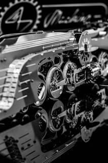 An intricate assembly of metallic gears and mechanical components with detailed reflections on a glossy surface. The scene includes circular cogs and patterns, suggesting a focus on machinery or a mechanical design project.