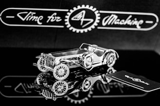 A highly detailed, metallic model of a vintage car is positioned on a reflective surface. The intricate design showcases gears and a classic car body. The background features the phrase 'Time for Machine' in a stylized script, offering a sense of branding or theme.