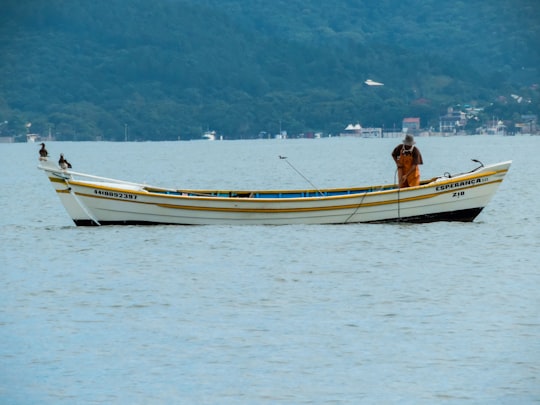 man in orange shirt riding on white and yellow boat during daytime in Florianópolis Brasil