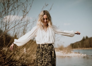 woman in white long sleeve shirt and black and white floral skirt standing on brown rock