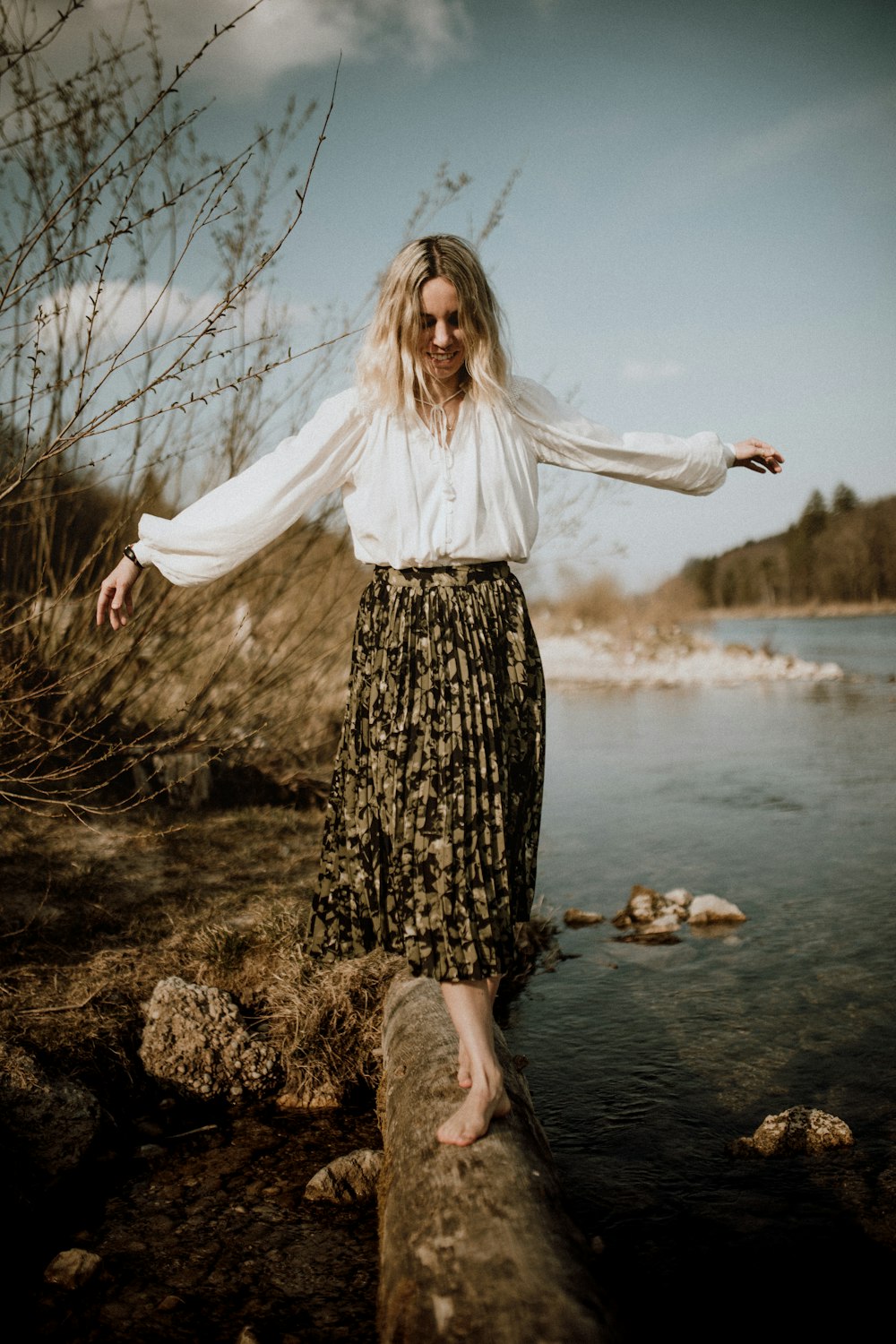 woman in white long sleeve shirt and black and white floral skirt standing on brown rock