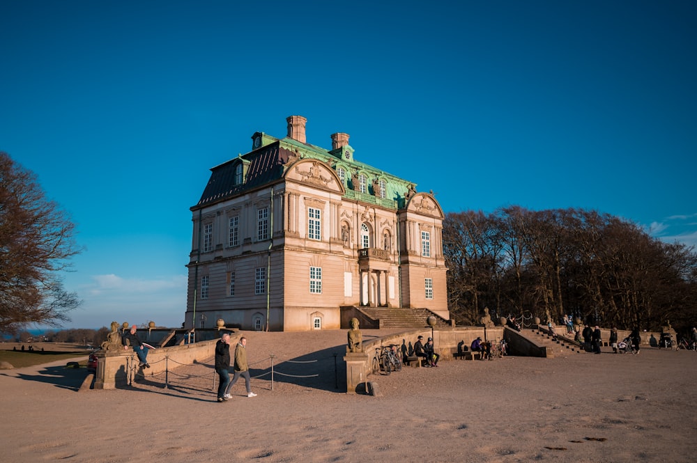 Menschen, die tagsüber auf braunem Sand in der Nähe von beigefarbenen Betongebäuden spazieren gehen