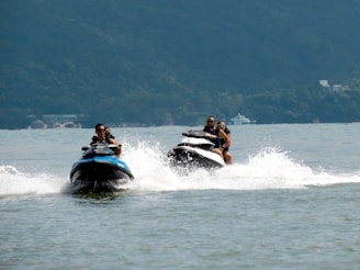 A joyful couple riding jet skis side by side with splashes of ocean spray around them.