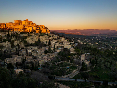 A scenic view of a Tuscan village with ancient stone buildings and a church tower at sunset.