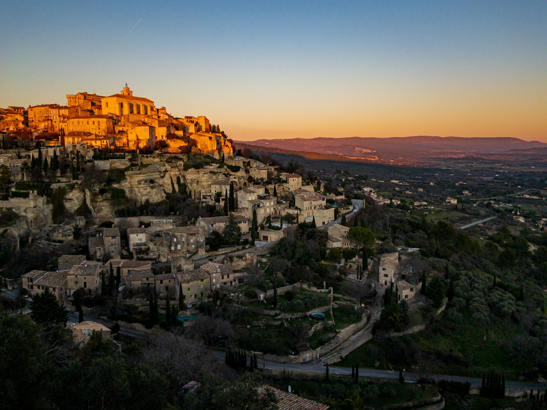 A warm Sicilian sunset over a rustic village with terracotta roofs and blooming bougainvillea.