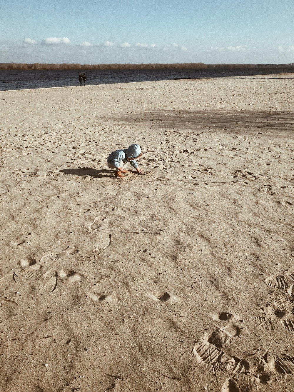 Person in blauen Jeans, die tagsüber auf braunem Sand spazieren geht