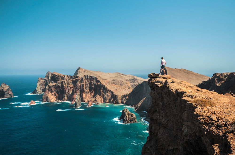 Hombre de pie en una formación rocosa marrón cerca del Mar Azul durante el día