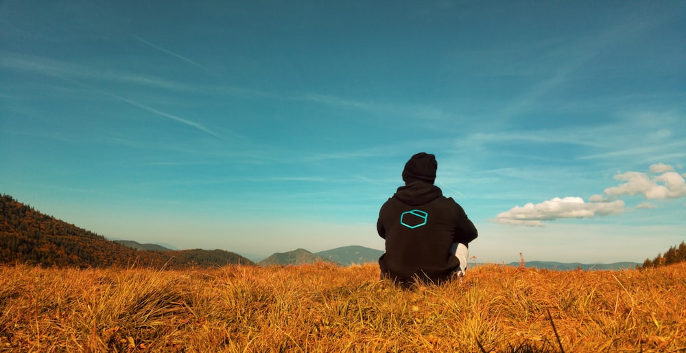 person in black hoodie sitting on brown grass field during daytime