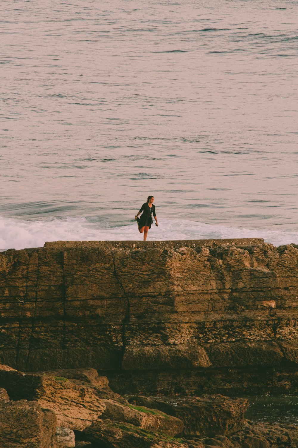 man in black jacket standing on rock formation near sea during daytime