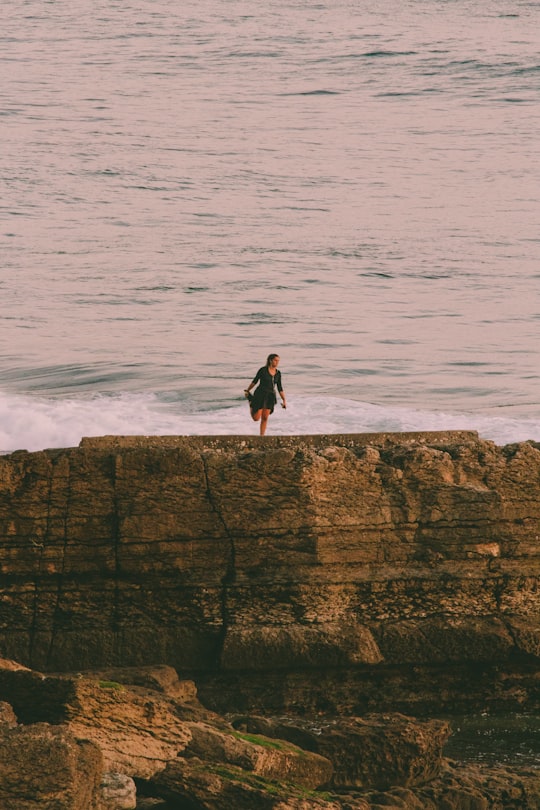 man in black jacket standing on rock formation near sea during daytime in Estoril Portugal