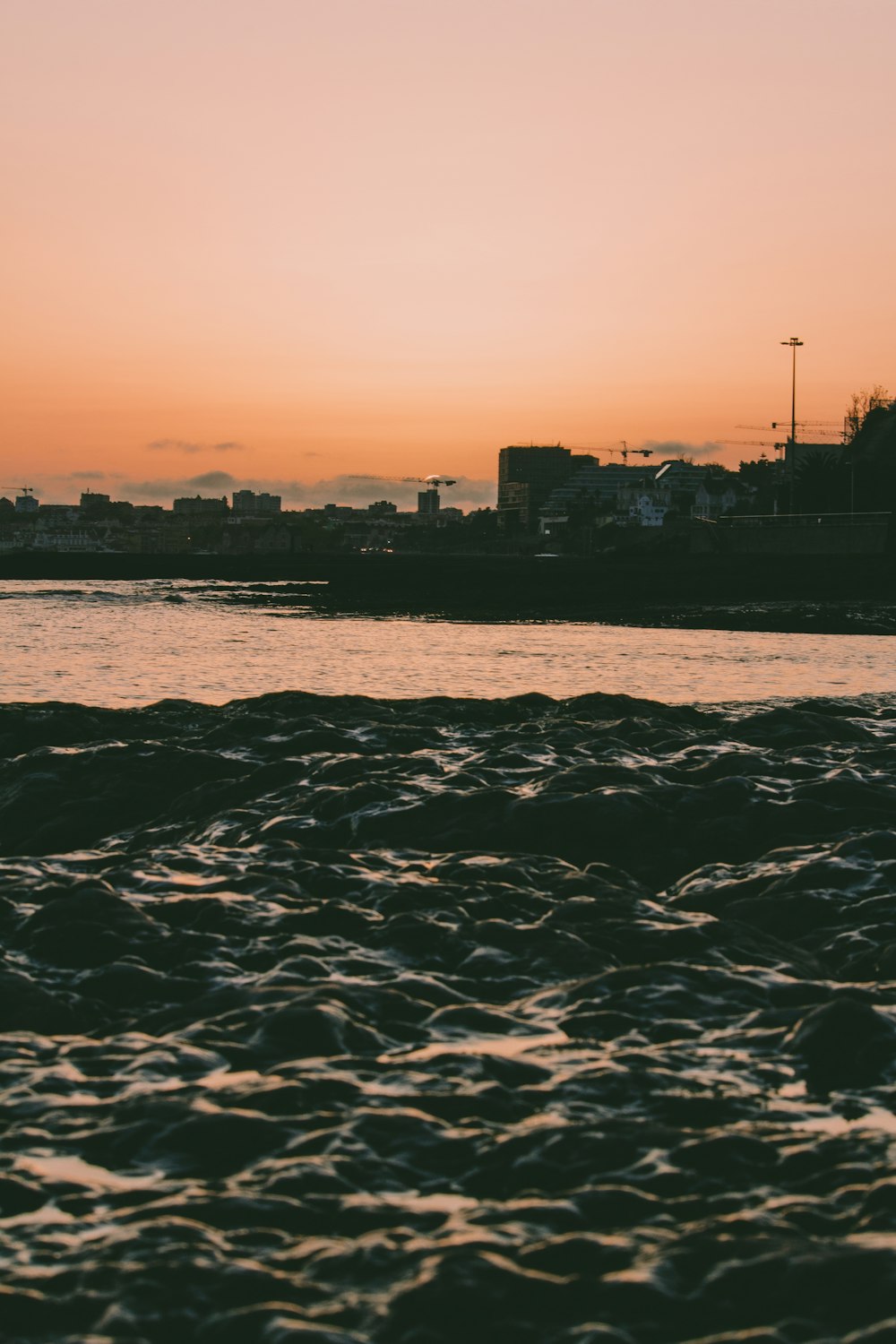 silhouette of city buildings near body of water during sunset