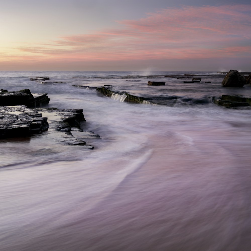 silhouette of rocks on sea shore during sunset