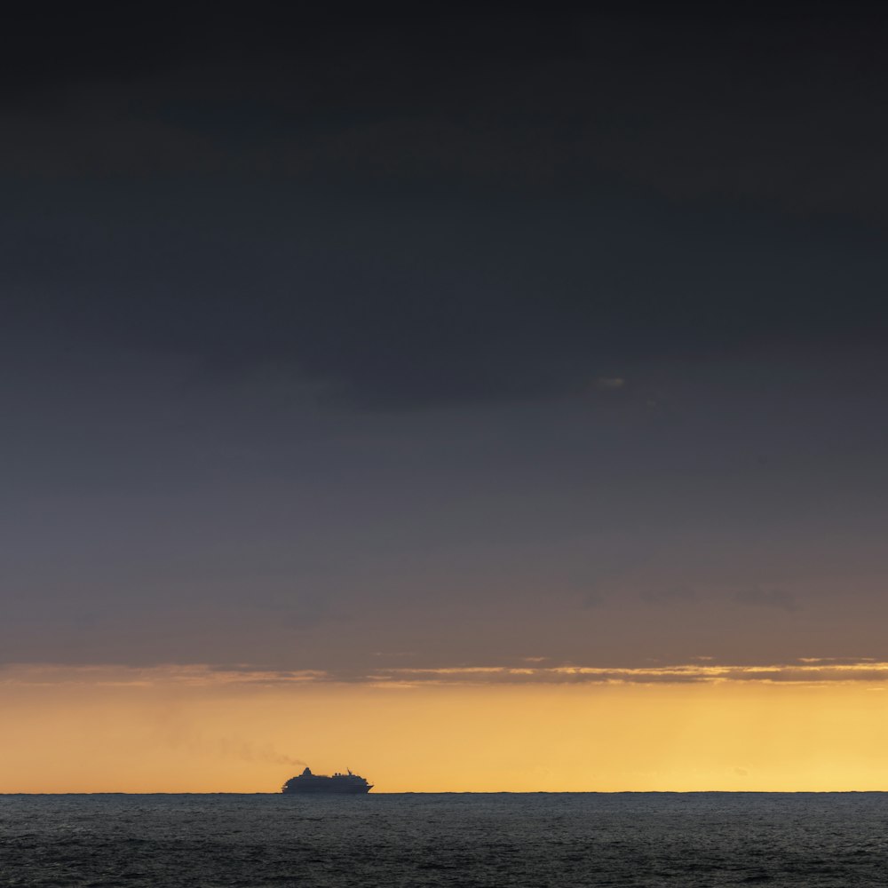 silhouette of a person on a rock in the middle of the sea during sunset