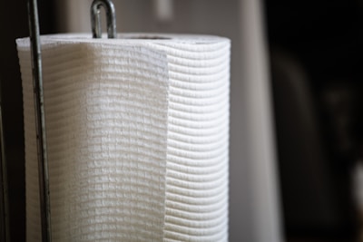 A close-up of a vertically oriented white paper towel roll, resting on a metal holder with a focus on the texture and material of the towel.