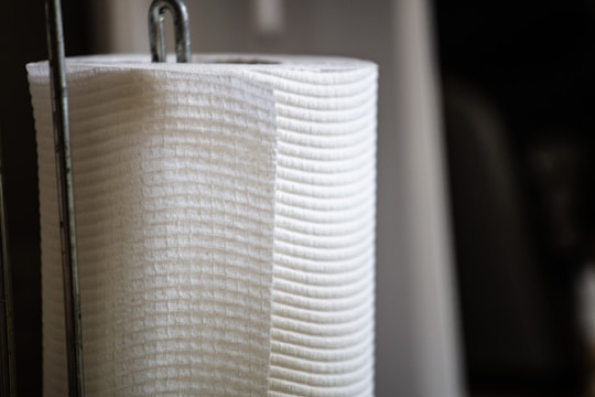 A close-up of a vertically oriented white paper towel roll, resting on a metal holder with a focus on the texture and material of the towel.