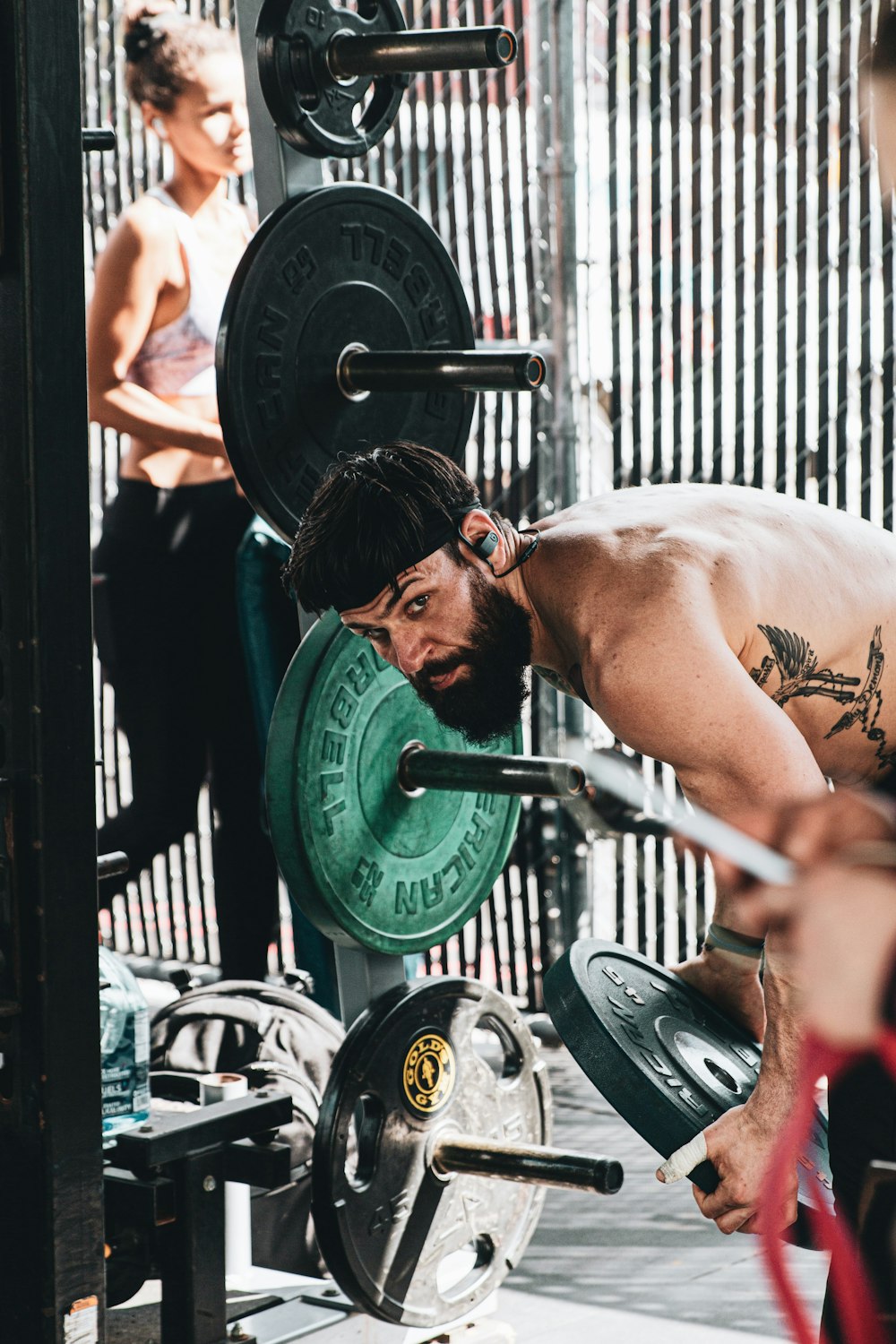 topless man carrying barbell in front of woman in black tank top