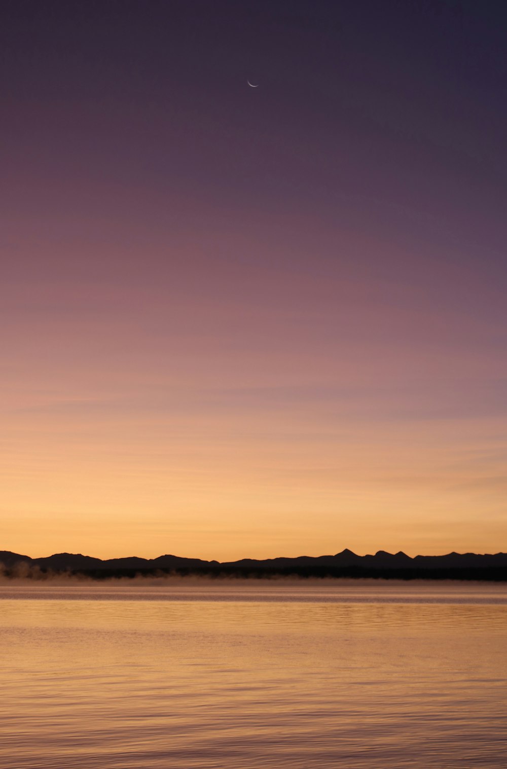 silhouette of mountain near body of water during sunset