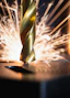 A gold metal drill bit cutting into a dark surface with bright sparks