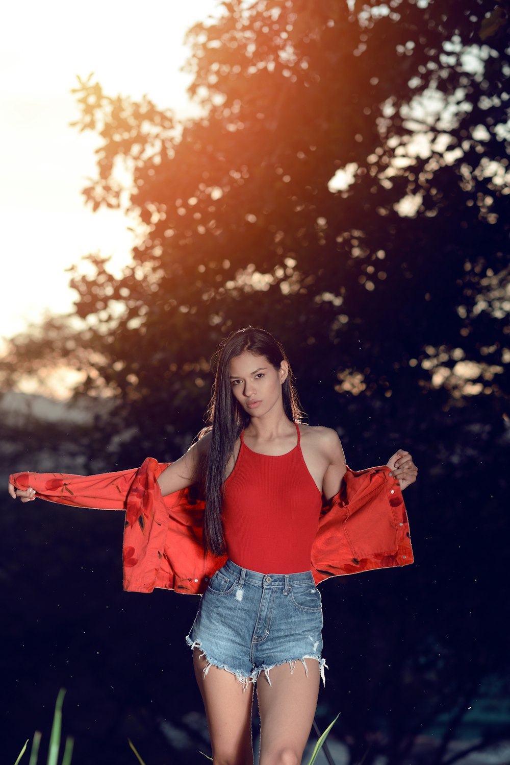 woman in red off shoulder shirt and blue denim jeans standing near trees during daytime