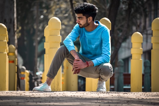 man in blue long sleeve shirt and brown pants sitting on concrete bench during daytime in Chandigarh India