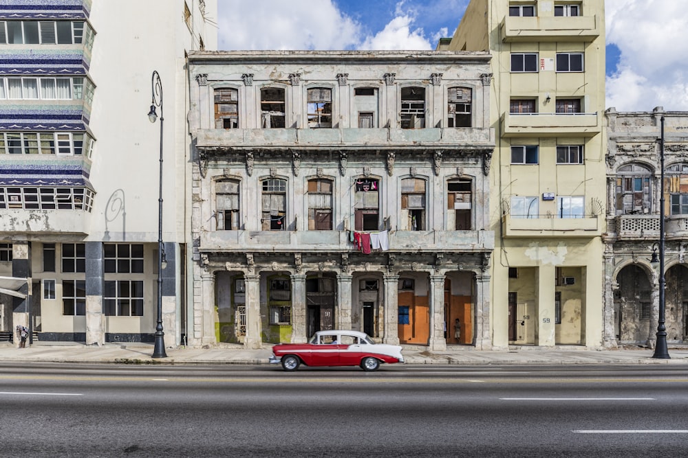 red coupe parked beside white concrete building during daytime