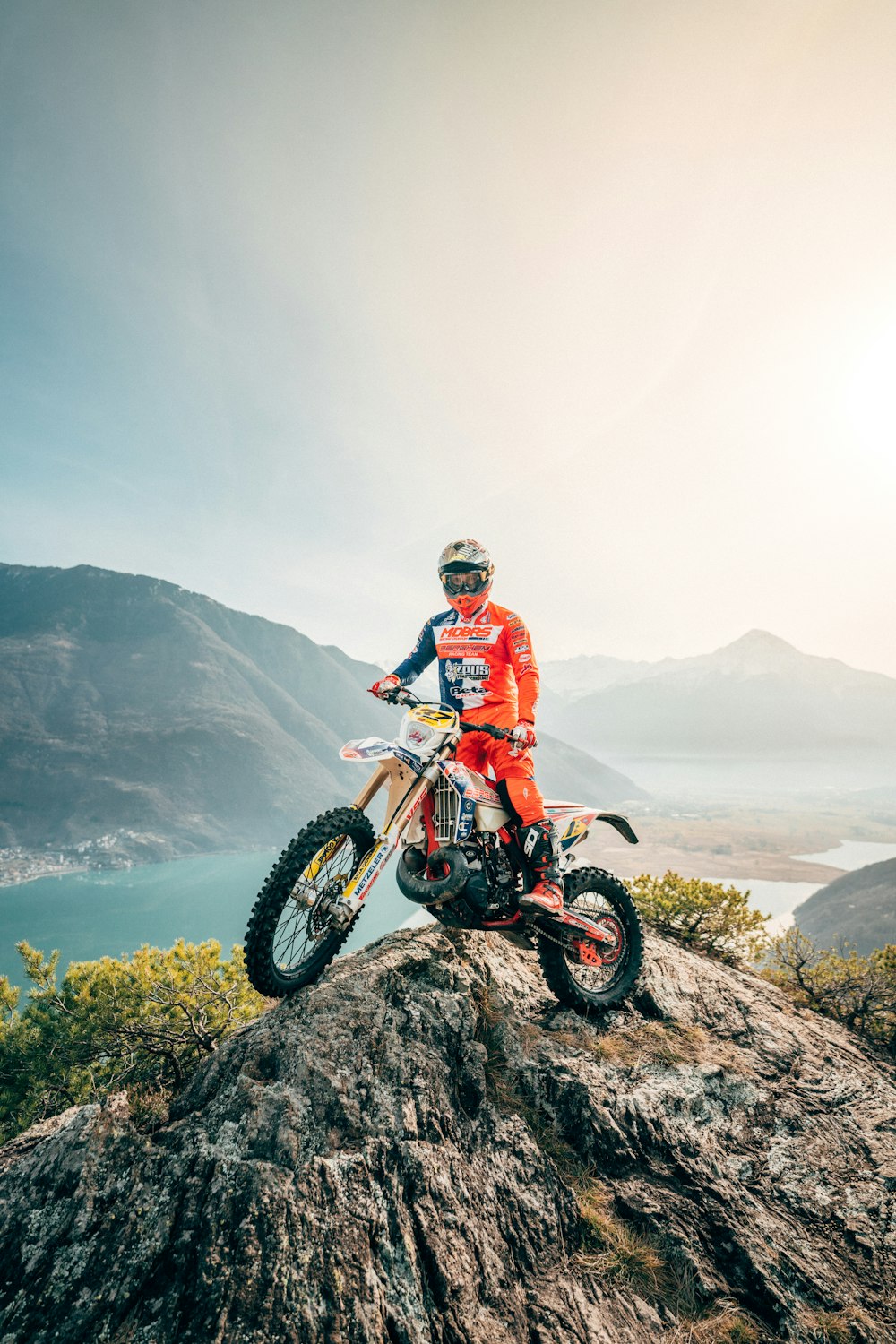 赤と白のモトクロススーツを着た男が昼間に山でモトクロスダートバイクに乗っている