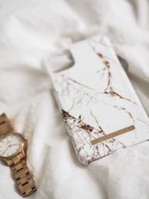 Luxury tech accessories like leather phone cases and smartwatches displayed on a marble surface.