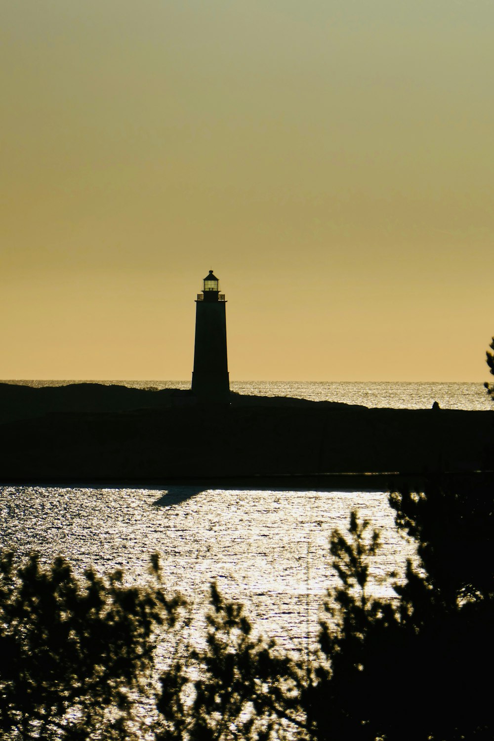 silhouette of lighthouse near body of water during sunset