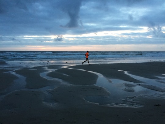 man in orange shirt and blue denim jeans walking on beach during daytime in Texel Netherlands