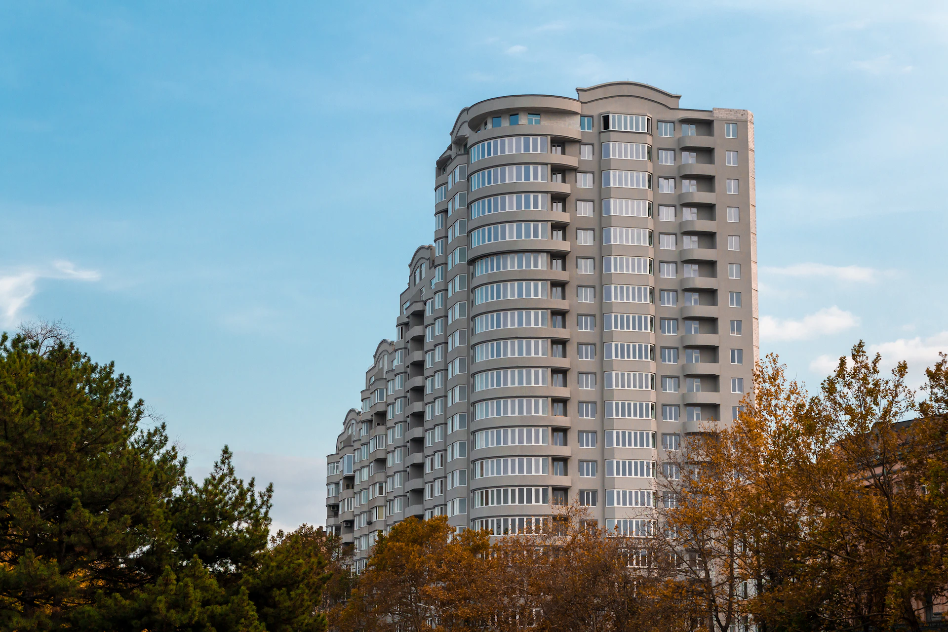 A sleek modern residential building with large glass windows reflecting the surrounding trees under a clear blue sky.