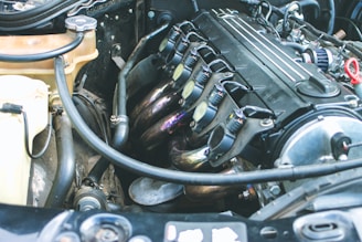A detailed view of a car engine with visible components including spark plugs, engine cover, various hoses, and wires. The engine appears clean and well-maintained, indicating it might be from a high-performance vehicle.