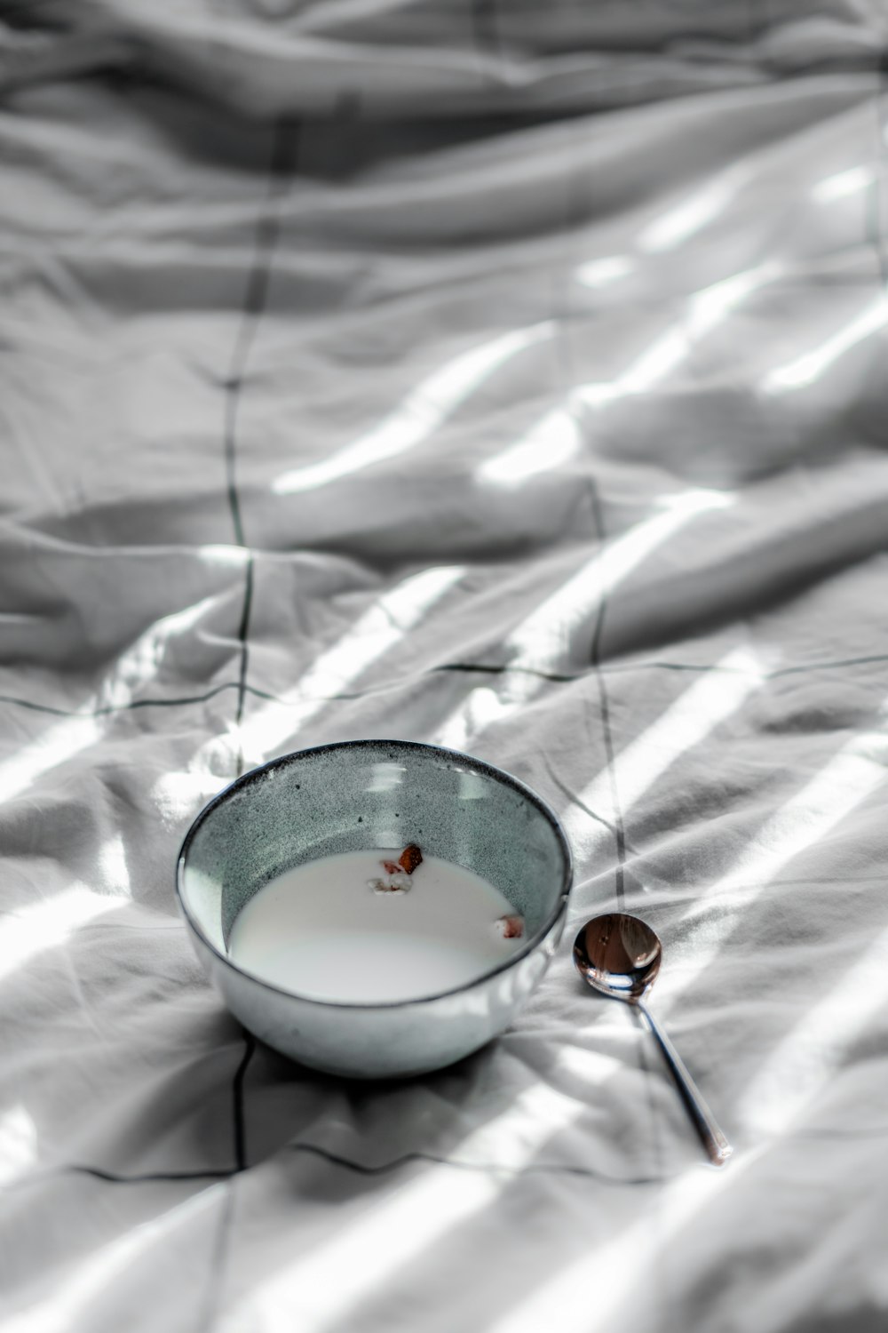 white ceramic bowl with silver spoon on white textile